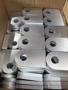 Wycinane laserowo metalowe elementy z otworami montażowymi ułożone w kartonie, precyzyjna obróbka stali